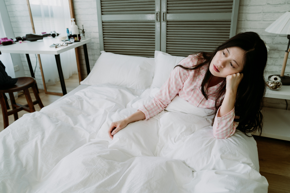 朝、ベッドの中で疲れた様子を見せる女性のイメージ、睡眠不足が心の余裕を奪うことを表す写真
